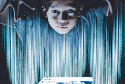 Digital composite image of boy gesturing over illuminated lighting equipment