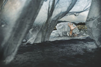 Cropped hand of person seen through plastic in lake