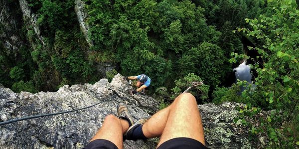 Low section of man sitting on top while person climbing mountain