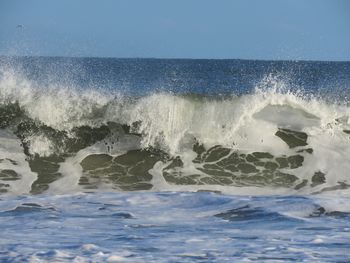 Waves splashing on sea against clear sky