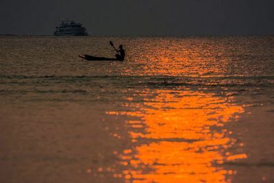 Silhouette man in sea against sky during sunset