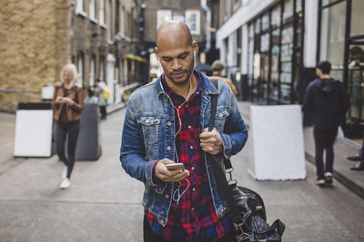 Mid adult man listening music through mobile phone on road in city