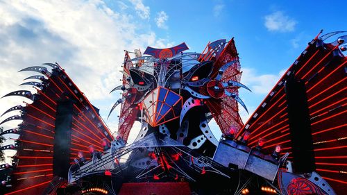 Low angle view of ferris wheel by buildings against sky