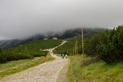 People walking on road by mountain against clear sky