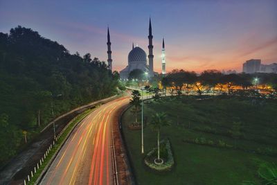 Light trails on road amidst buildings against sky