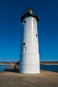 Lighthouse by sea against clear blue sky