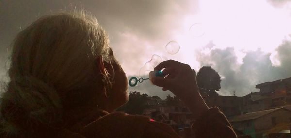 Rear view of woman blowing bubbles against sky at sunset