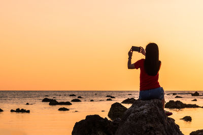 Man photographing sea against sky during sunset