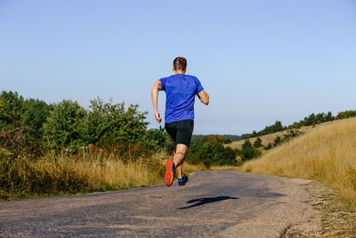 Rear view of man walking on road against clear sky