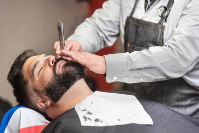 Midsection of barber shaving customer beard in salon