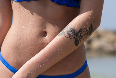 Midsection of woman with tattoo on hand at beach