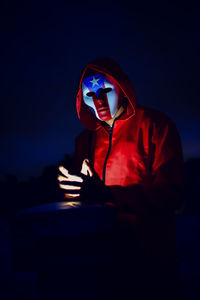 Man looking at illuminated camera against sky at night