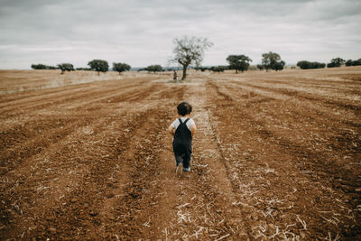 Rear view child running through plowed fields