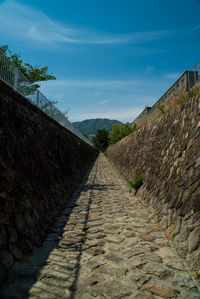 Footpath by wall against sky