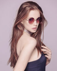 Portrait of woman wearing sunglasses against pink background