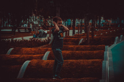 Full length of elementary boy covering ears while standing at park