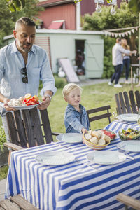 Boy assisting father while arranging food on table in back yard