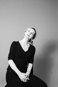 Thoughtful woman sitting on chair against gray background