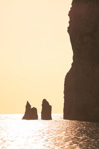 Silhouette rock formations by sea against clear sky
