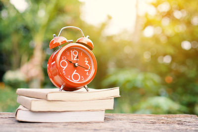 Orange alarm clock and book on table outdoors