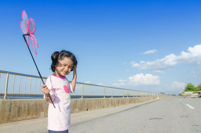 Portrait of girl holding pinwheel toy while standing on road against sky