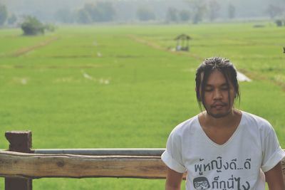 Thoughtful man sitting on bench against rice field 