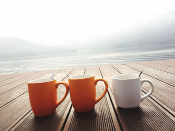 Coffee cup on table by sea against sky