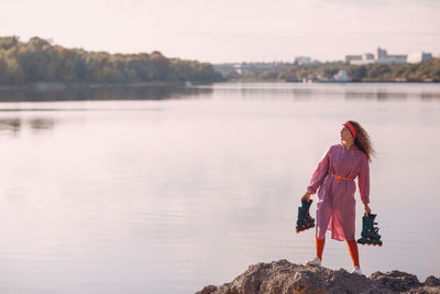 Woman standing on rock looking at lake against sky