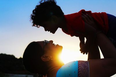 Side view of woman carrying son against clear sky during sunset