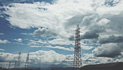 Low angle view of electricity pylon against cloudy sky