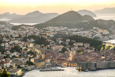 Aerial view of city by sea and mountains against sky