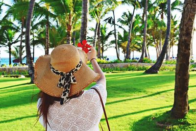Rear view of woman wearing hat while holding flower in park at beach