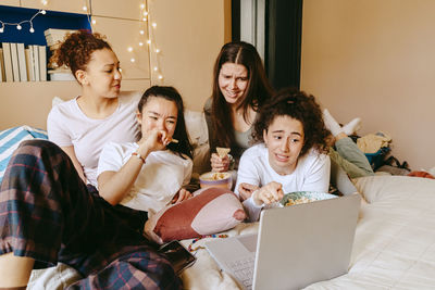 Female friends making faces while watching movie on laptop at home