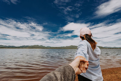 Woman holding boyfriend hand at beach against sky