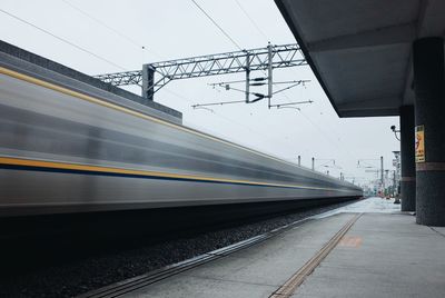 Train speeding by railroad station platform against sky