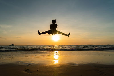 Silhouette man jumping on beach against sky during sunset