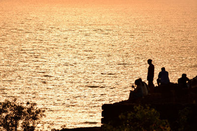 Silhouette people by sea against sky during sunset