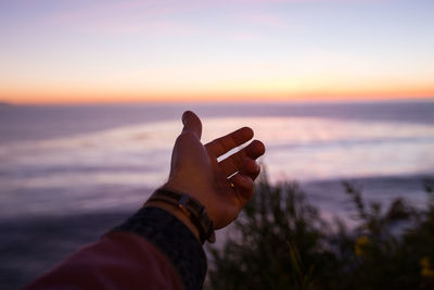 Close-up of woman hand on beach against sky during sunset
