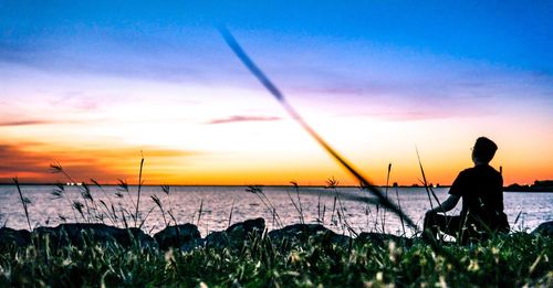 Silhouette man fishing on beach against sky during sunset