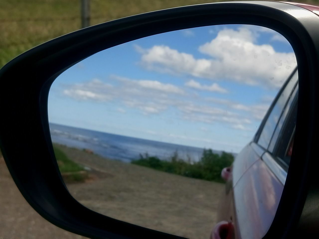 REFLECTION OF SKY SEEN THROUGH SIDE-VIEW MIRROR