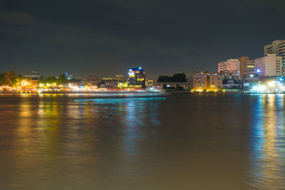 Illuminated city by river against sky at night