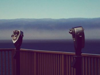 Coin-operated binocular at observation point by sea and mountains against sky
