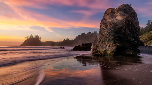 Rock formation on beach against sky during sunset