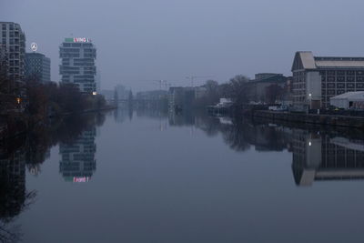 Buildings by river against sky in city