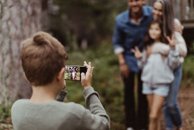 Boy taking picture of family with mobile phone while standing in backyard