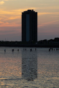 Sea by buildings against sky during sunset