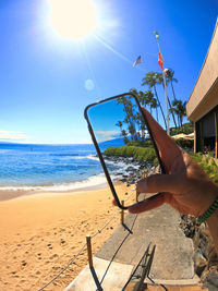 Cropped hand of person photographing sea with mobile phone against sky