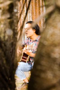 Man playing guitar seen through tree trunk