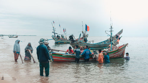 Fishermen by moored boat in sea against sky