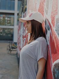 Side view of woman looking away while standing against wall